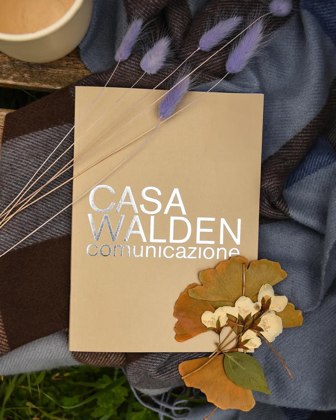 Foto ambientata tra fiori secchi e plaid del Quaderno Walden beige con elegante logo di Casa Walden Comunicazione laminato argento impresso sulla copertina
