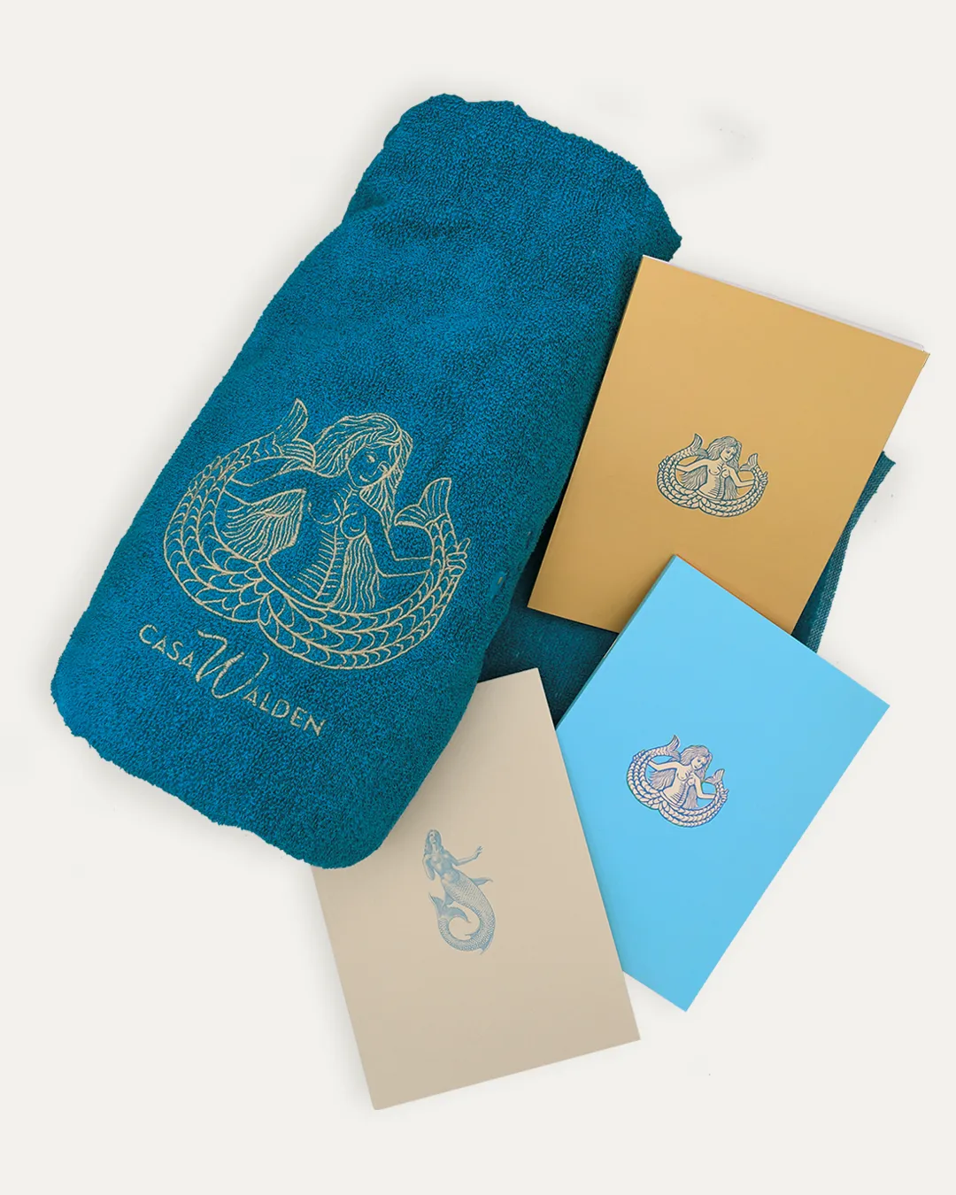 Bundle Sirene 1 Collage degli Still-life dei prodotti della collezione Sirene by Walden quali: telo mare Ondina azzurro con sirena bicaudata ricamata a mano e logo Casa Walden, i quaderni Ondina in versione beige e azzurro con illustrazione della serena bicadauta, e quaderno Partenope con copertina in carta martellata beige e icona azzurra di una sirena