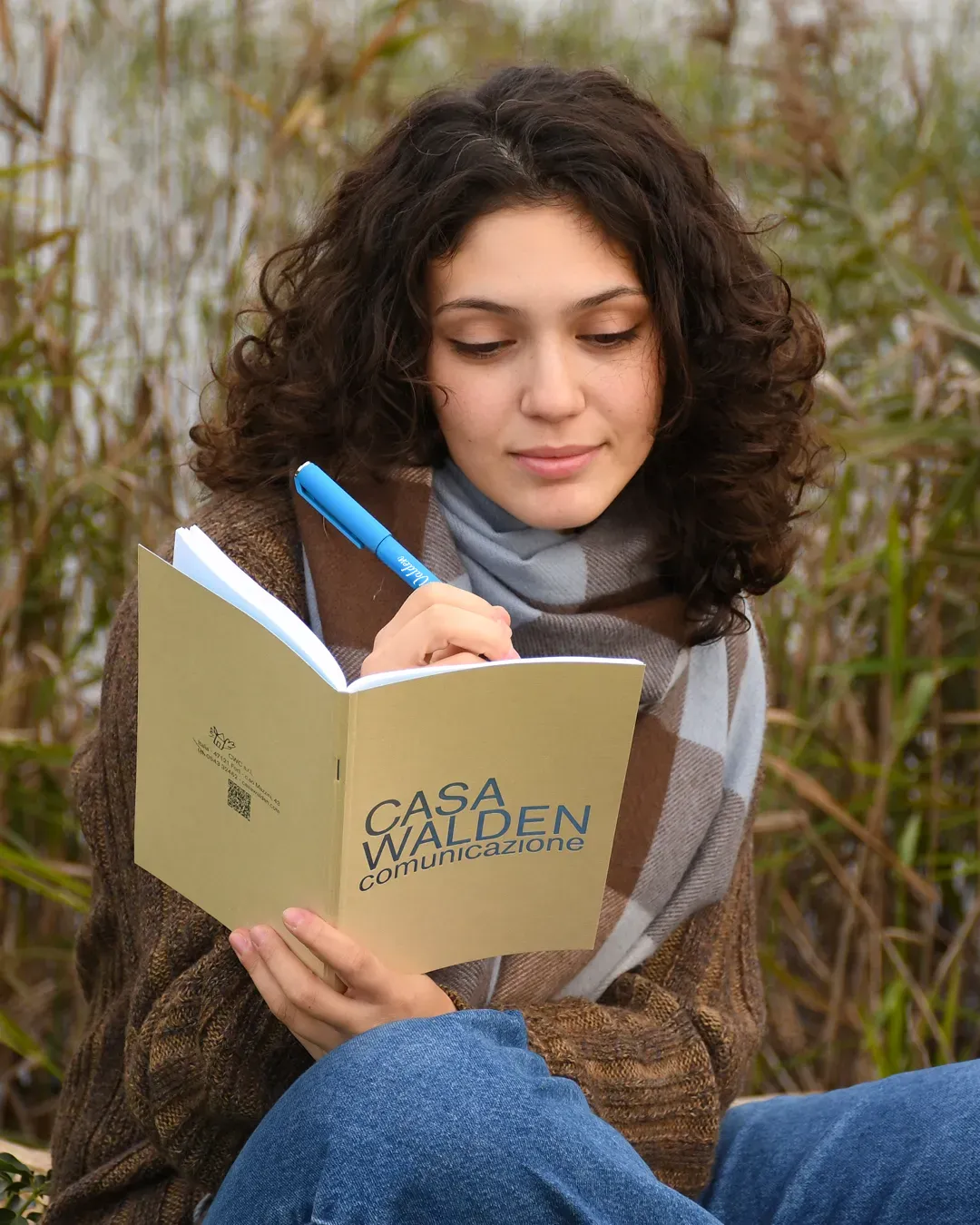 Foto ambientata in natura di una ragazza che scrive sul quaderno Walden con penna gel ‘LightBlue’ dell'omonima linea byWalden