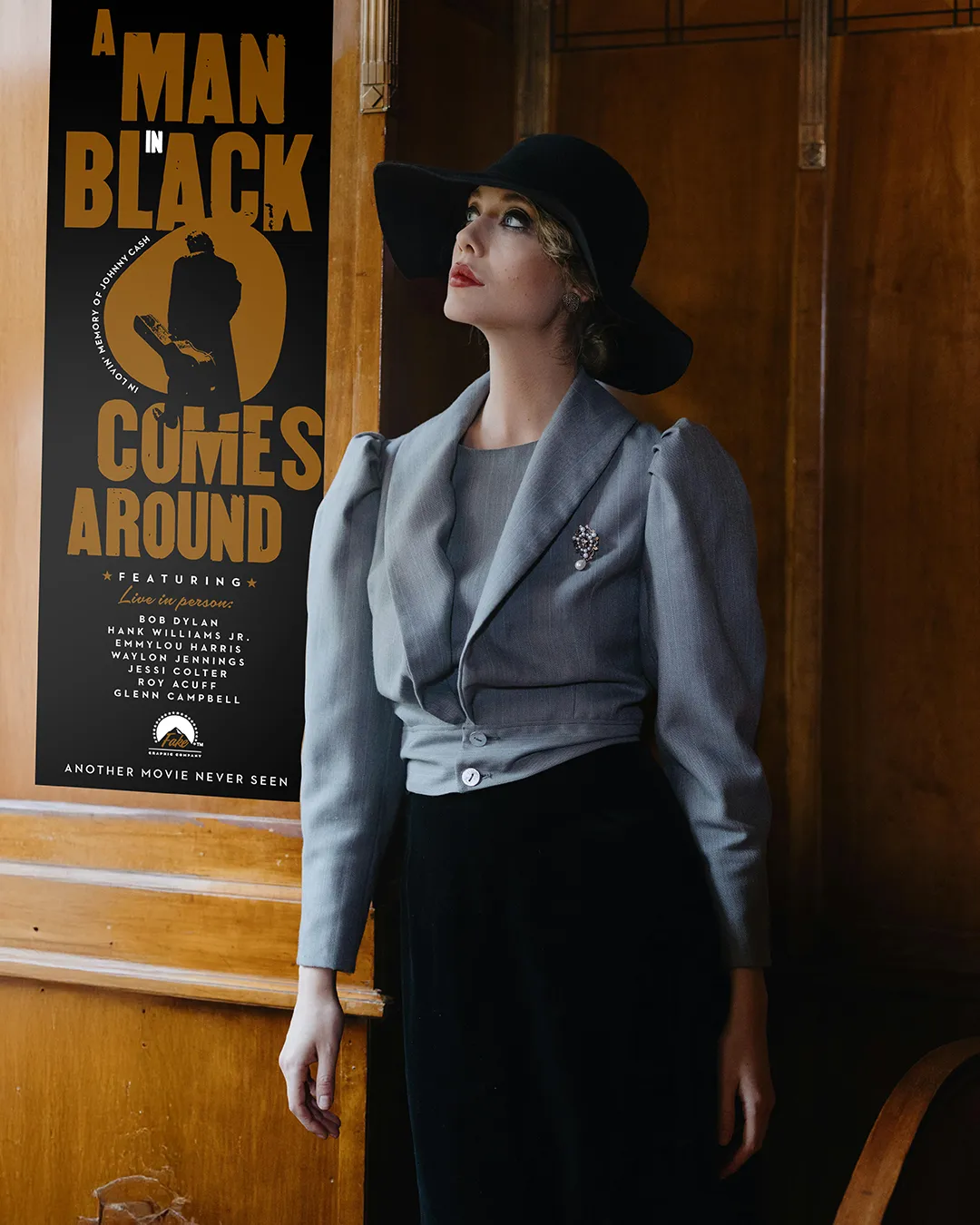 Donna in abiti eleganti degli anni '20 '30 del 900, con cappello nero, poggia su una parete in legno a fianco a un poster cinematografico con sfondo nero e la scritta “BLACK COMES AROUND” in arancione