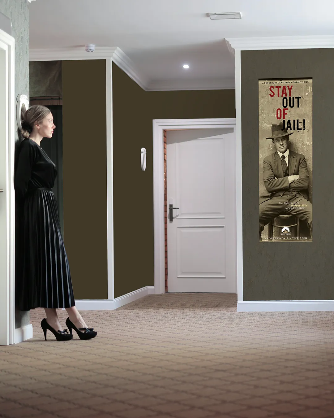 Donna in abito elegante nero di velluto, in piedi in un corridoio, osserva un grande poster cinematografico appeso al muro con la scritta “STAY OUT OF JAIL!” e la foto in bianco e nero di un uomo seduto con cappello e completo.