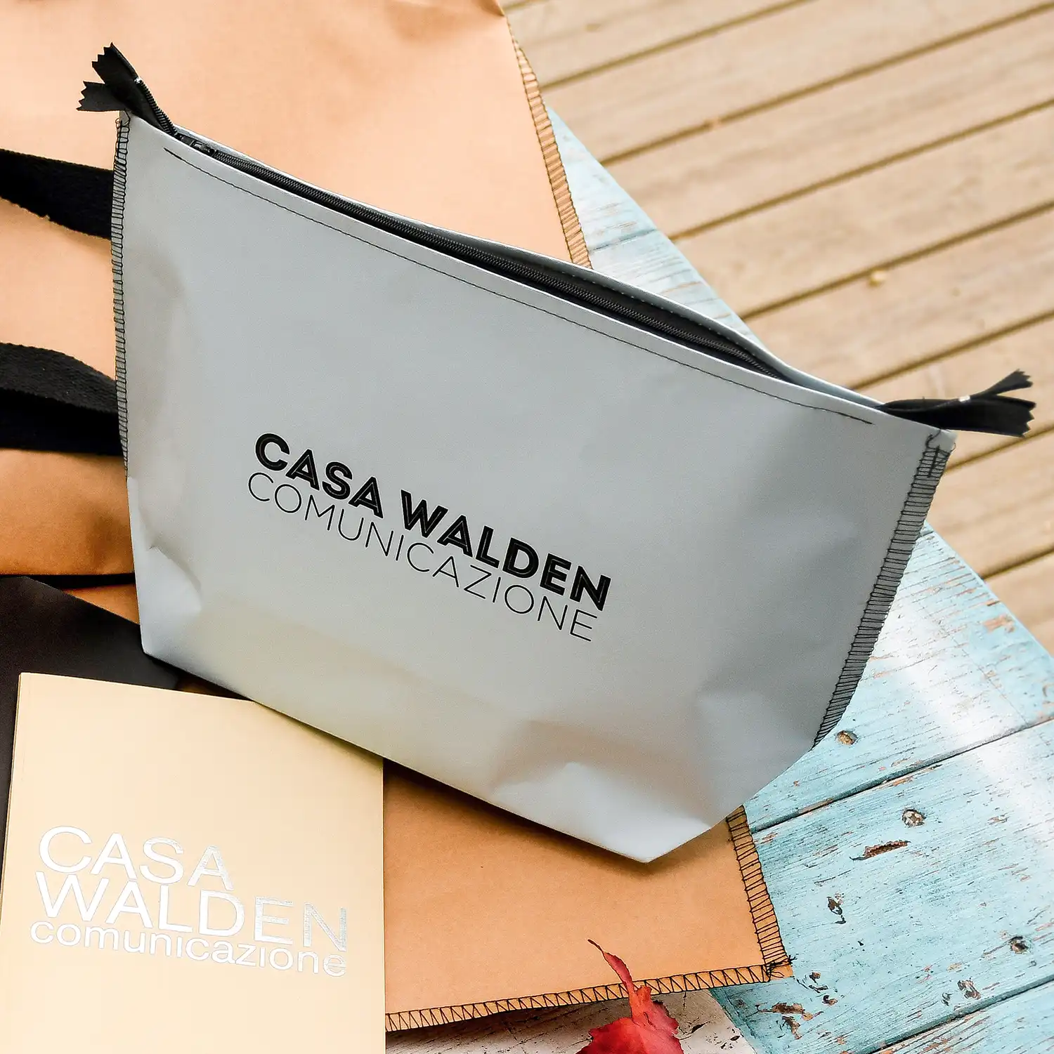 pochette Walden ambientazione foto ambientata su panche di legno della Pochette Walden artigianale in carta 100% naturale celeste con zip, cuciture e marchio Casa Walden Comunicazione in nero
