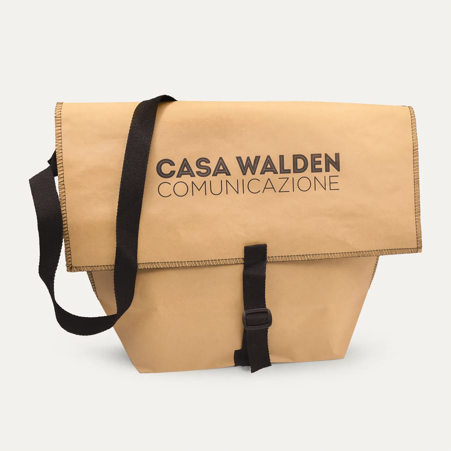 Still-life della messenger bag La Postina della collezione Walden, realizzata in carta naturale cucita con fibia e tracolla in tessuto nero con al centro il logo di Casa Walden Comunicazione scritto in nero a stampatello.