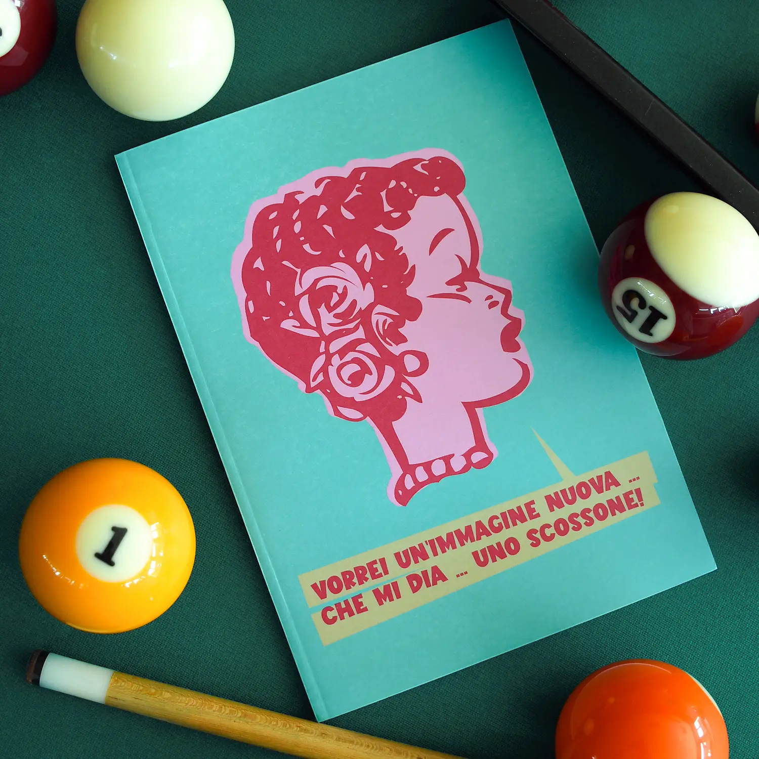 quaderno anni ’50 Lola ambientazione Scatto fotografico del Quaderno Lola posizionato su tavolo di biliardo, la copertina verde riporta una testa cartoon di donna anni '50 e la scritta a stampatello ‘Vorrei una immagine nuova che mi dia uno scossone!’