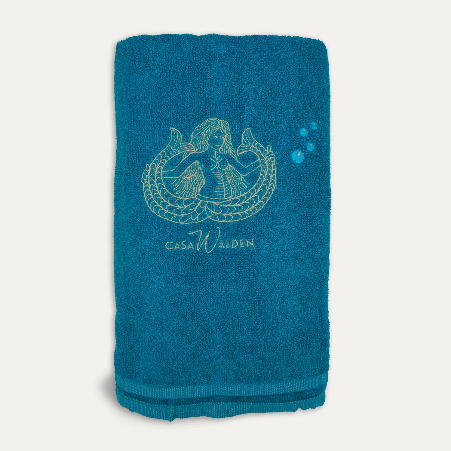 Telo Marea Telo mare, avvolto su se stesso, di color azzurro con ricamo in evidenza di una sirena bicaudata, tre bollicine e logo di Casa Walden.