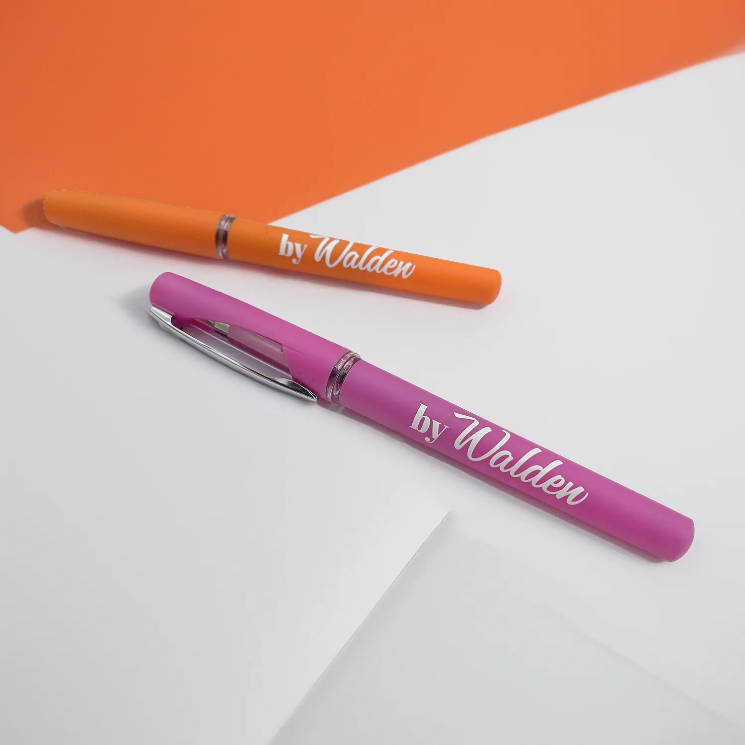 Penne By Walden Due penne gel di colore rosa e arancio, con logo bianco 'byWalden', tappo protettivo con finestrella trasparente e clip metallica per aggancio, poggiate su dei fogli bianchi