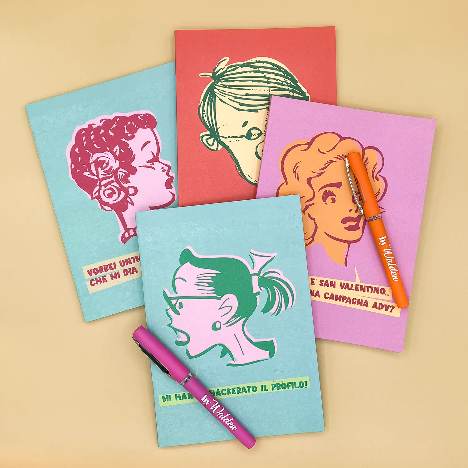 collezione 1950s, quaderni con Penne Due penne gel di colore fucsia e arancio, con logo bianco 'byWalden', tappo protettivo con finestrella trasparente e clip metallica per aggancio, poggiate sui quaderni Lola, Berto, Dolly e Patty della collezione 1950's byWalden.